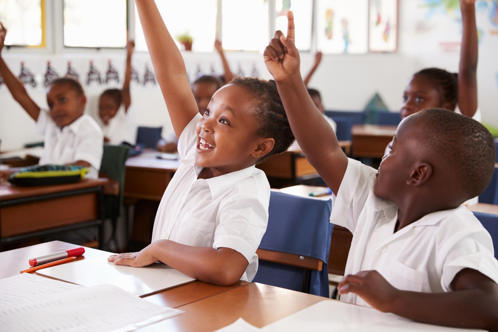 Happy children raising their hands in class
